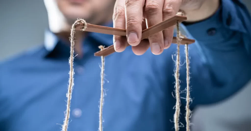 Male hand holding puppet strings to demonstrate wounded feminine energy (manipulation)